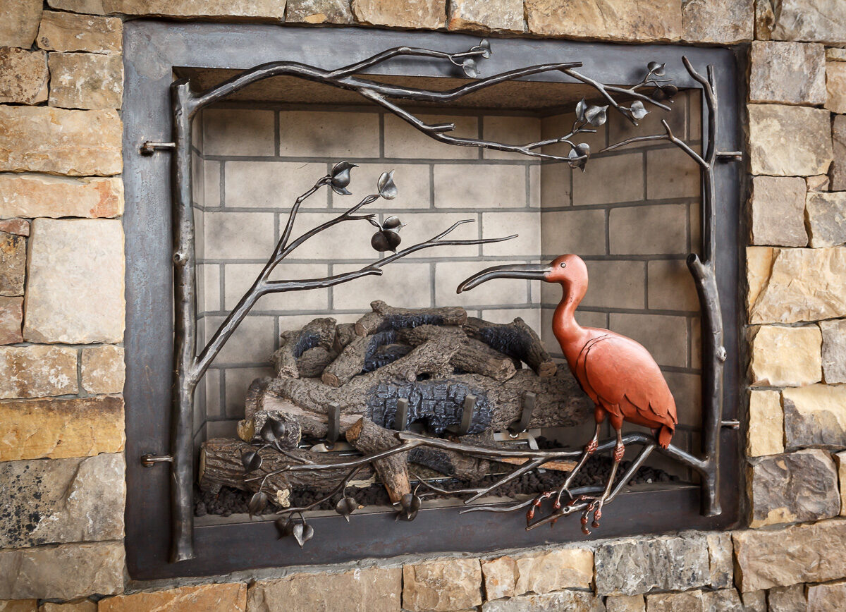 Nature-inspired hand-forged fire screen with a bird among branches for a lakefront home